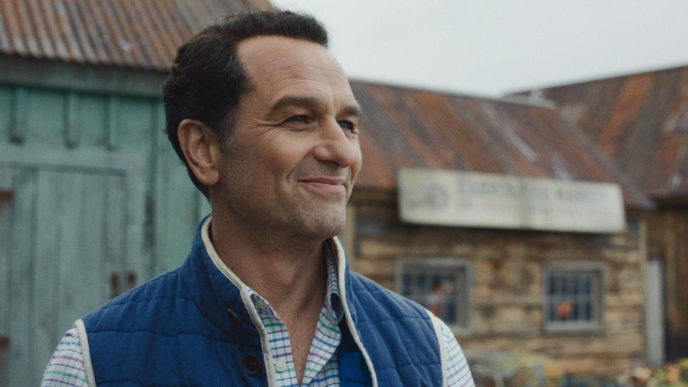 Matthew Rhys in a striped shirt and blue body warmer in a still from Widow's Bay