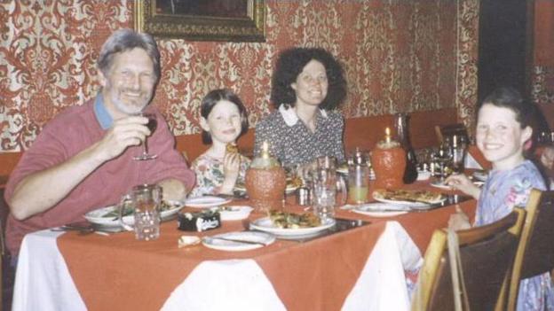 The Russell family, pictured at an Italian restaurant in early 1996. Youngest child Megan is sat between her parents, Shaun and Lin Russell, with Josie sat across the table. There are plates of food and drinks on the table and all four are smiling at the camera. 