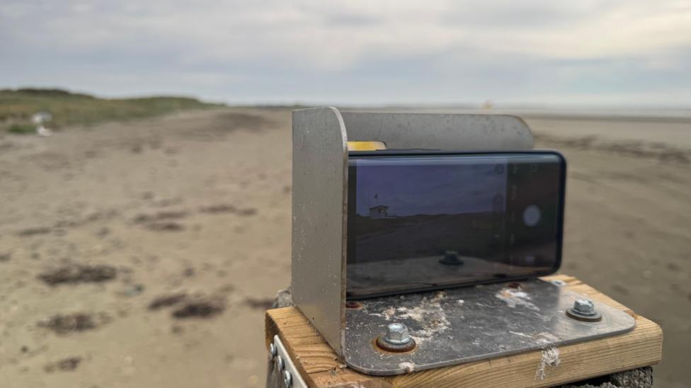 A metal phone holder on top of a post on a beach.