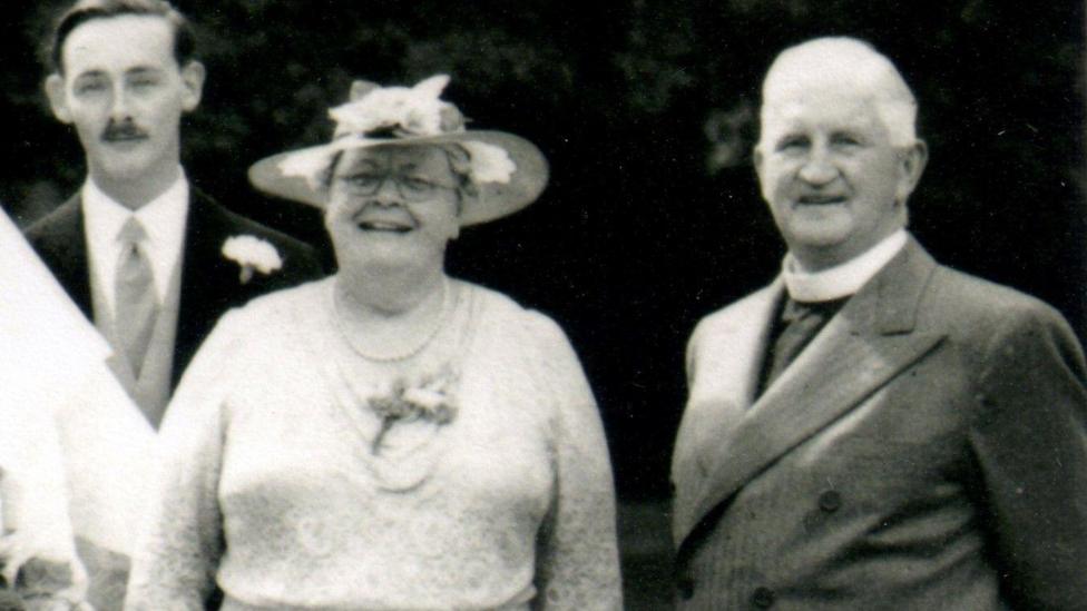 A black and white image of Eileen Elgar with Alfred, her husband, and another man behind them. She is wearing a hat.
