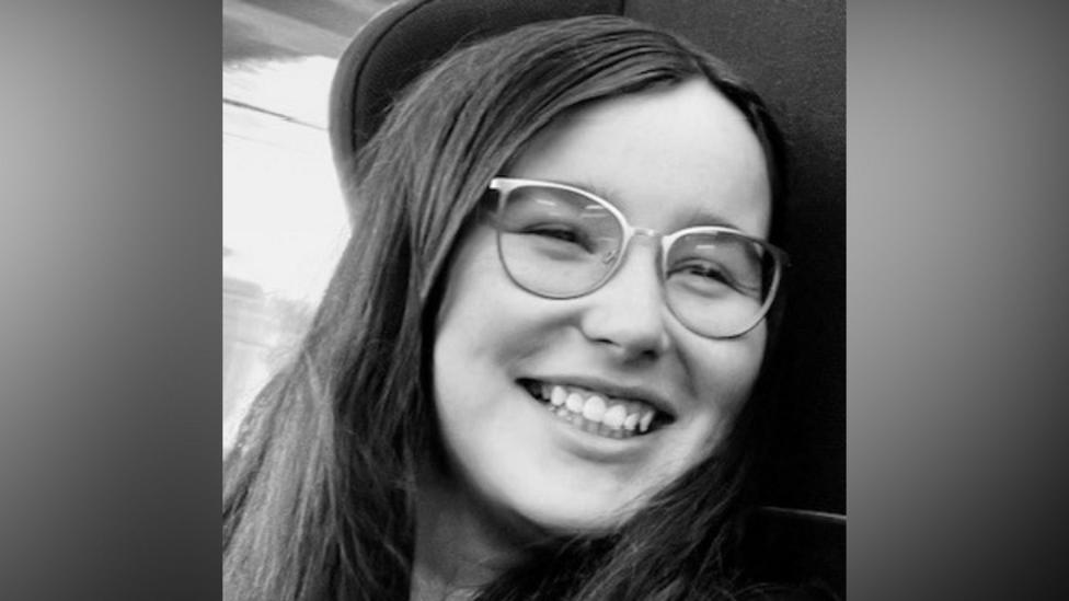 Close-up black-and-white photograph of Jess Turnbull. She is smiling as she looks to her left. She has long dark hair and is wearing glasses.