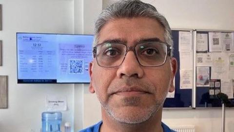 A man with grey hair wearing glasses and blue shirt