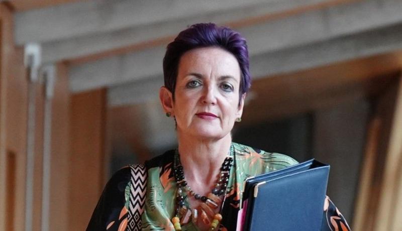 Angela Constance, Cabinet Secretary for Health and Care, arriving for First Minister's Questions at the Scottish Parliament in Holyrood, Edinburgh. She has short purple hair, is carrying a folder for paperwork and is wearing chunky necklaces.