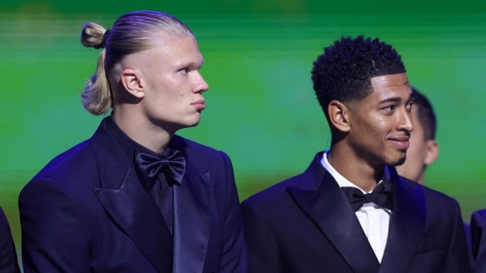 Haaland on the left and Bellingham on the right are in black tuxedos at the event and are standing in front of a green backdrop.