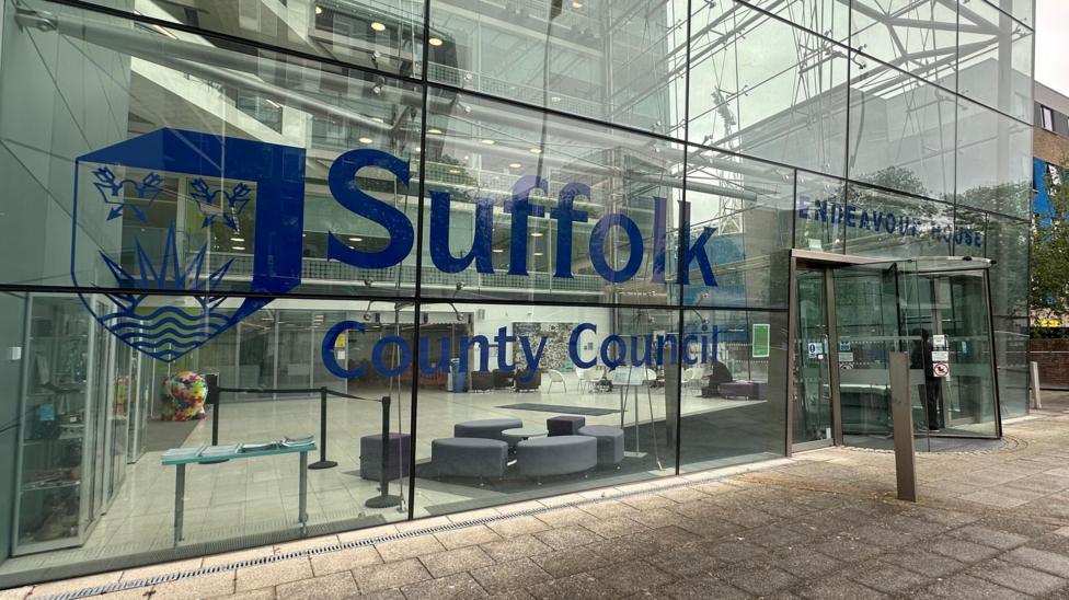 A general view of the main entrance at Suffolk County Council's headquarters. It is a glass building with the name of the council on the windows in blue along with its logo.