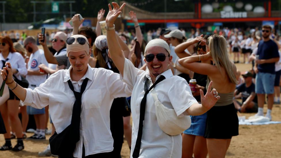 Fans dressed as Pitbull in white shirts and bald caps dance in the crowd.