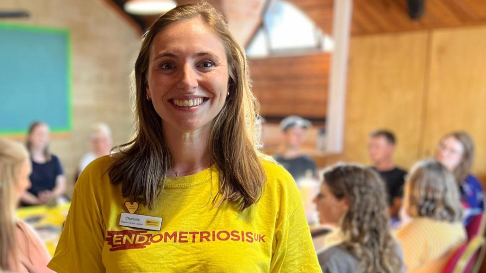 Charlotte smiles at the camera, wearing a bright yellow top with the words 