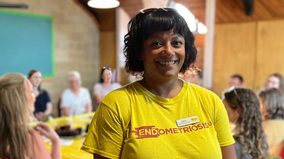 Jakia smiles at the camera, wearing a bright yellow top with the words 