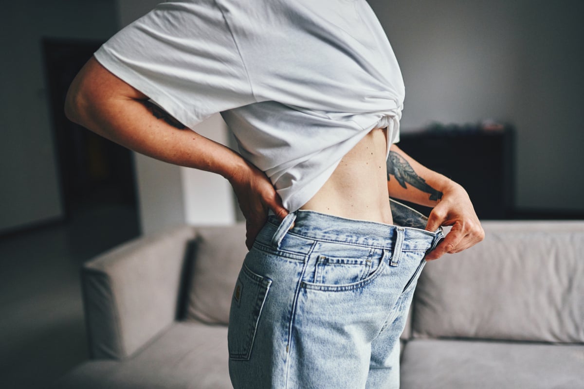 An individual demonstrating noticeable weight loss by wearing loose jeans