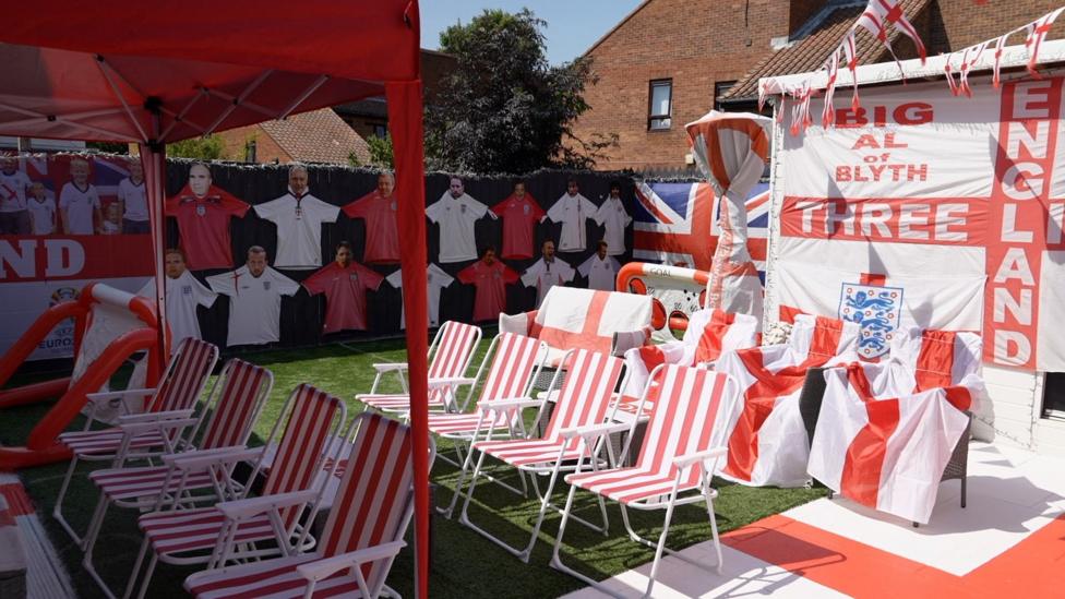 An alternate view of the garden, which shows he has created a line-up of England's team on his fence by tacking up kit shirts and printing photos of the players' heads. We can also see rows of red-and-white striped chairs, which will be used by his audience to watch the match.