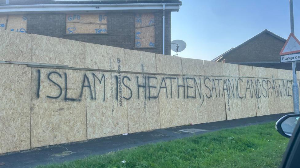 Spray-painted in black lettering on the chipboard hoarding is the message 'ISLAM IS HEATHEN, SATANIC AND SPAWNED'