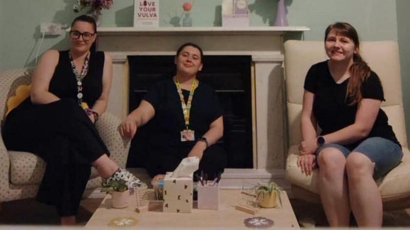 Three women wearing black sit in a living room.