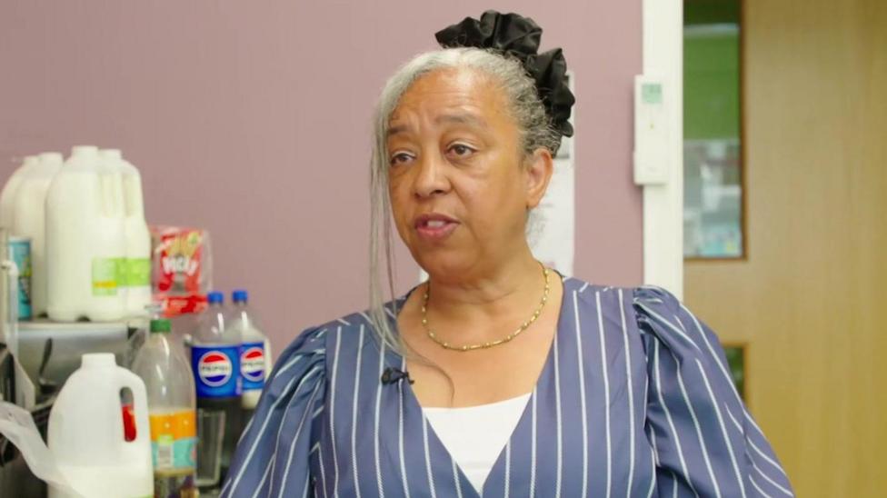 A close-up shot of Doreen Davies wearing a striped top and speaking inside the Pecan charity cafe kitchen.