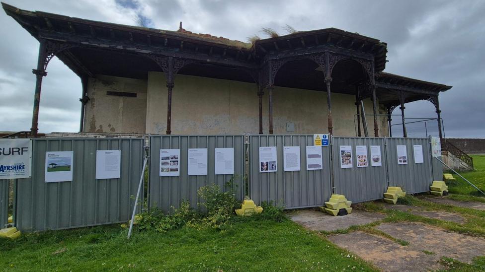 A dilapidated bandstand building, with fences set up around it. 