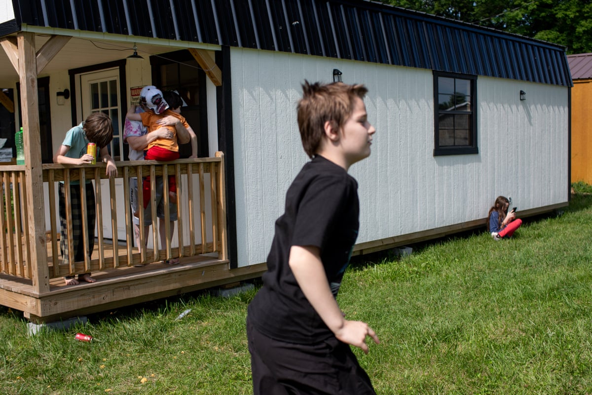 Children play while a woman holds a small child on the porch of a small home.