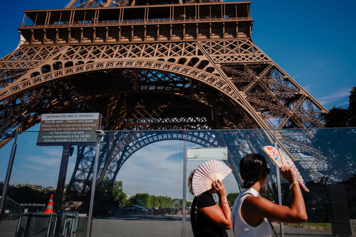 Two tourists shade themselves with fans as they walk past the base of the Eiffel Tower