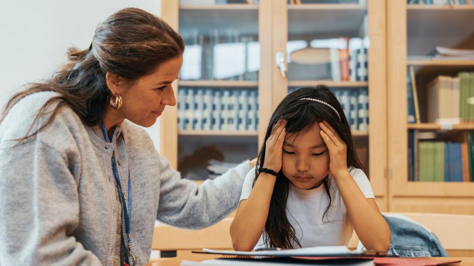 Female counselor consoling girl sitting with head in hands at a school