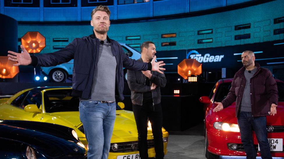 Flintoff with arts outstretched on the top Top Gear set, in front of Paddy McGuinness and Chris Harris and two cars