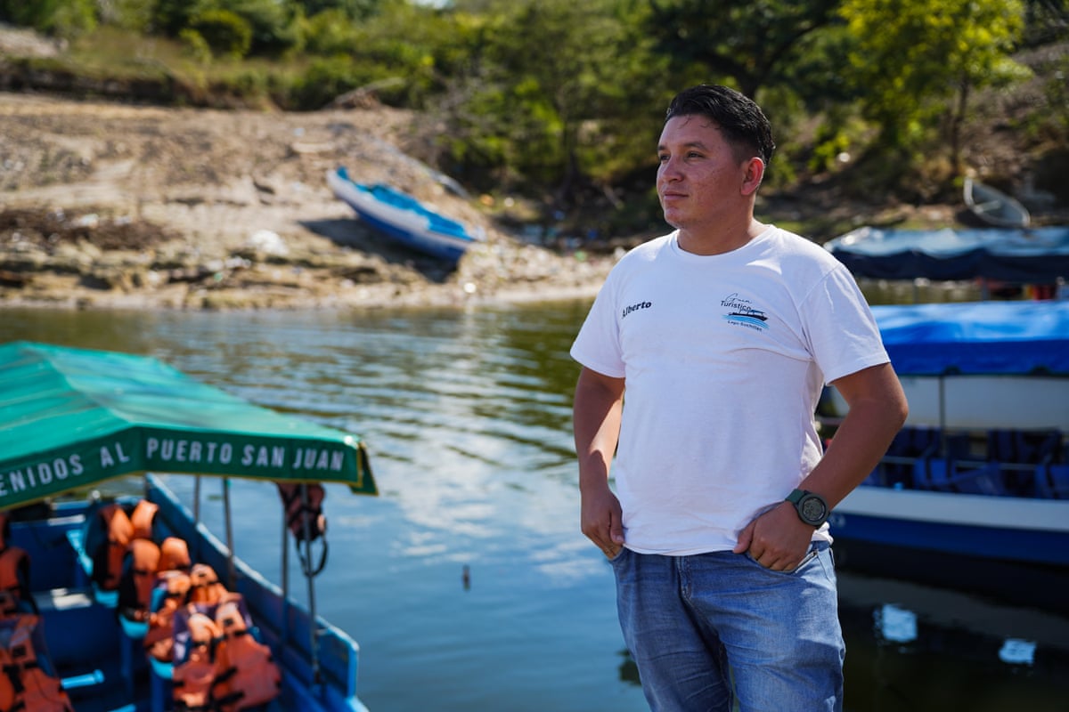 A young Latino man standing by water with pleasure boats