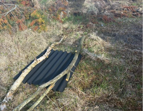 A black metal sheet held down by two long sticks on green grass