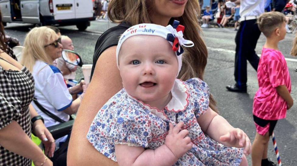 A baby is wearing a hairband that says 