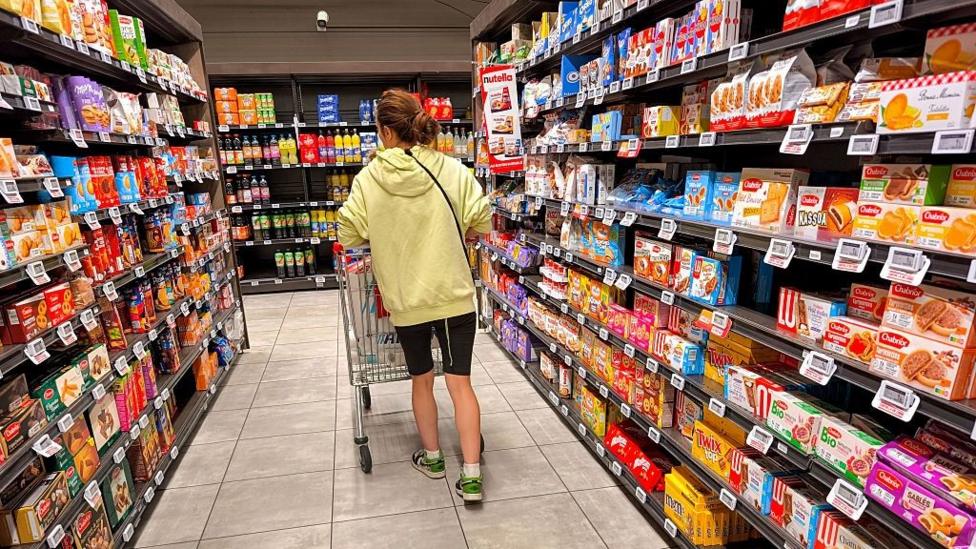 A woman shops pushes her shopping cart through a cake and biscuit aisle at an Intermarché supermarket in France.