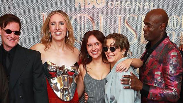 Cast members posing at a premiere with arms over each other's shoulders and smiling and laughing