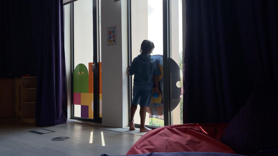 Eight-year-old Azuriah staring out of a window. The boy is pictured from the back and there is a card design on one of the long windows.