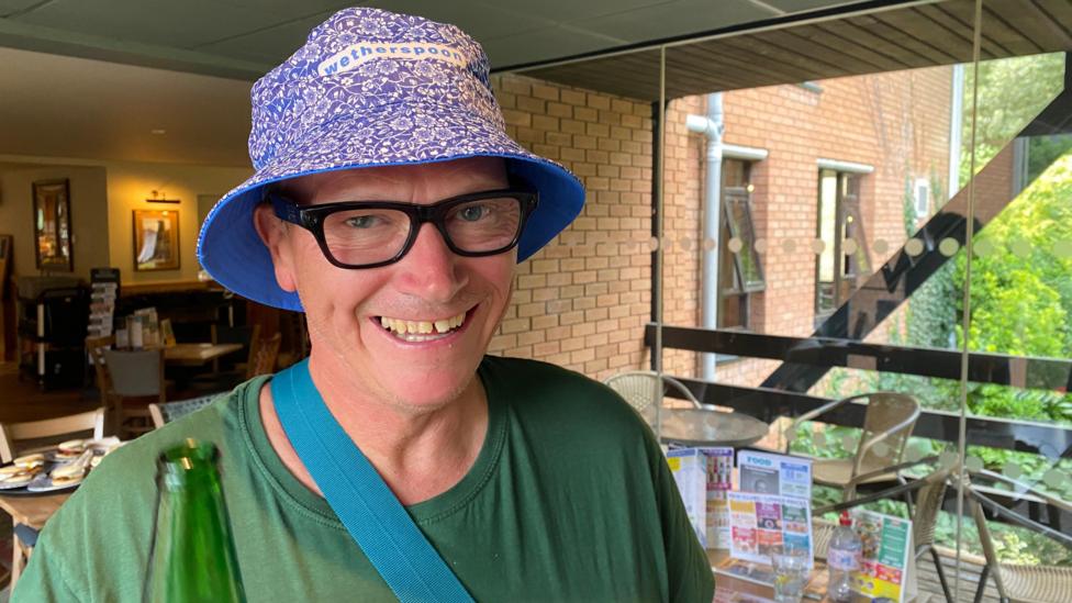 A man with glasses, green T-shirt and a lilac flowery bucket hat.