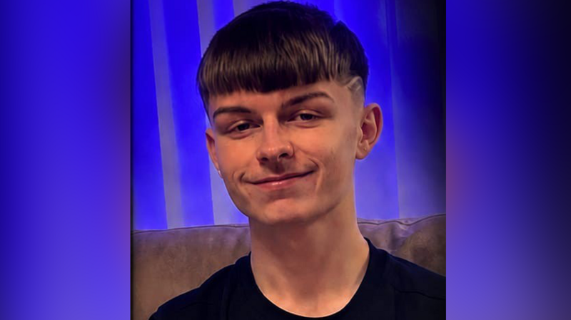 A teenage boy smiling at the camera. He has short brown hair and a black t-shirt on.
