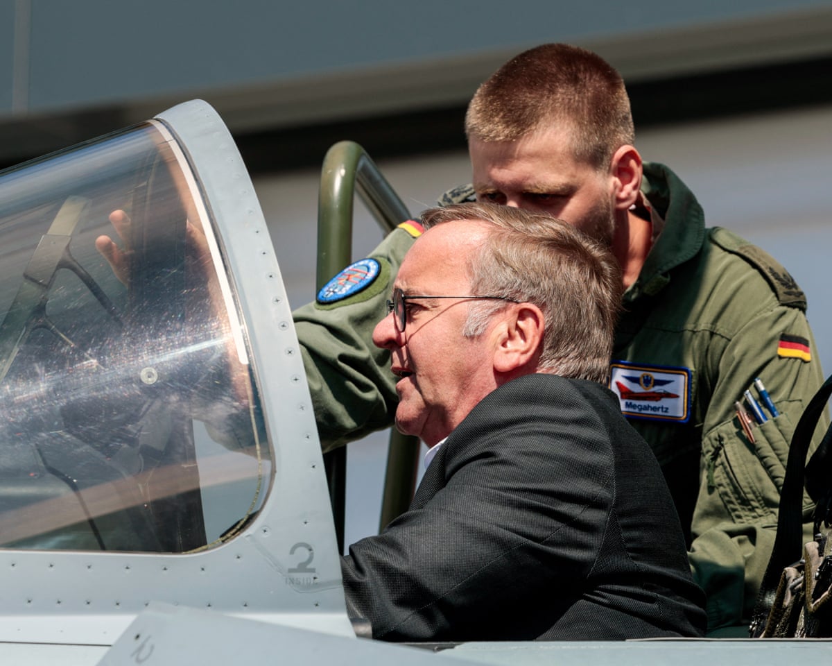 Boris Pistorius sits inside a cockpit as a soldier leans over him.