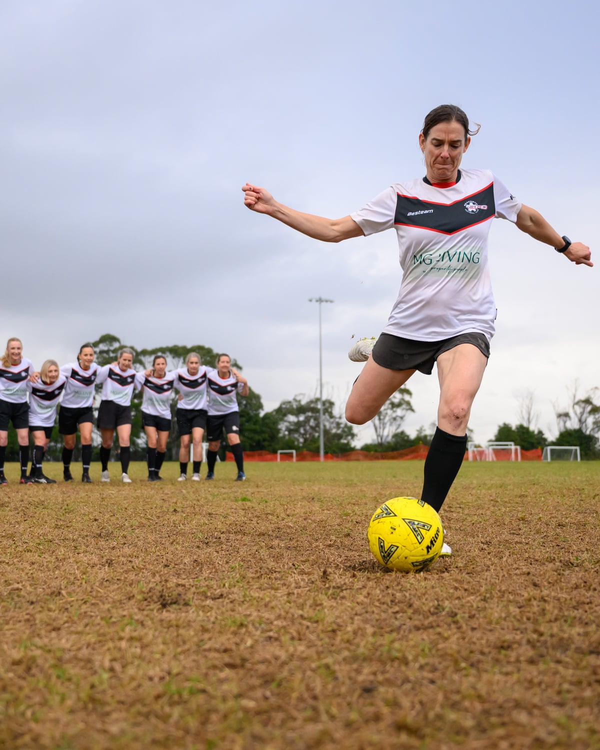 Holbeck kicks the ball as her team link arms behind her