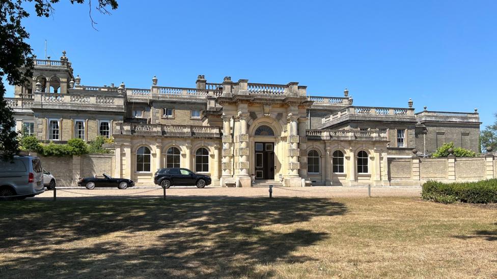 The outside of Shrubland Hall – a historic, English country house. The sky is blue with no clouds.