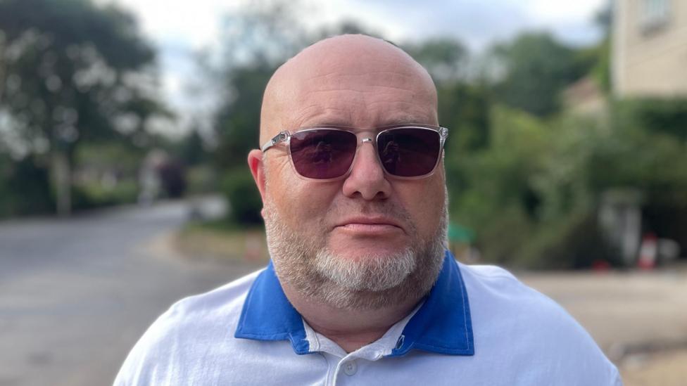 A head and shoulders image of a man. He is wearing glasses and a white and blue polo shirt.