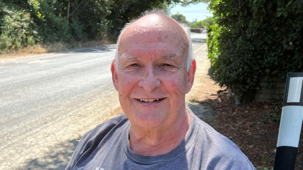 A man wearing a grey T-shirt and smiling. There is an empty road behind him.