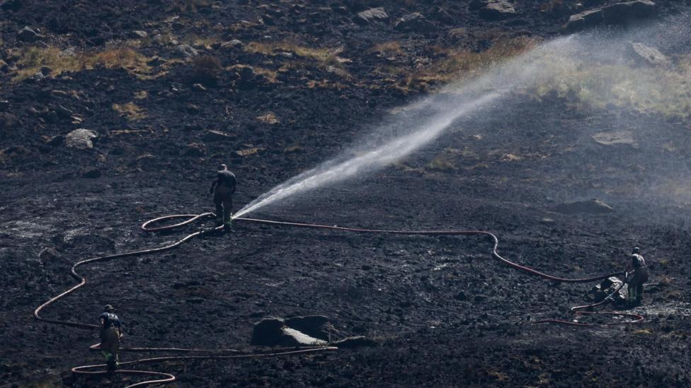 Firefighter on Dove Stone spraying jets of water over the moorland.