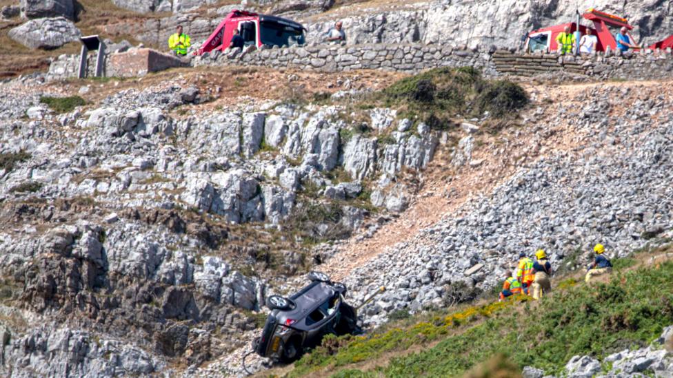 Crews work to recover the vehicle which is lying upside down and pointing back up the slopes