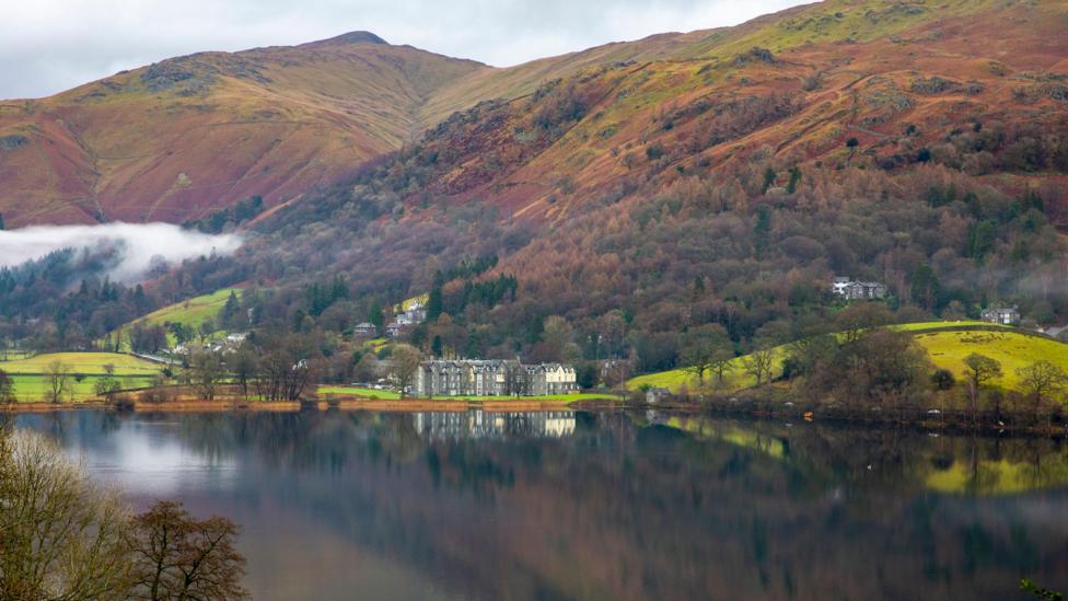 The village of Grasmere as seen from across the lake. Mist hangs over the trees and fells rise in the background.
