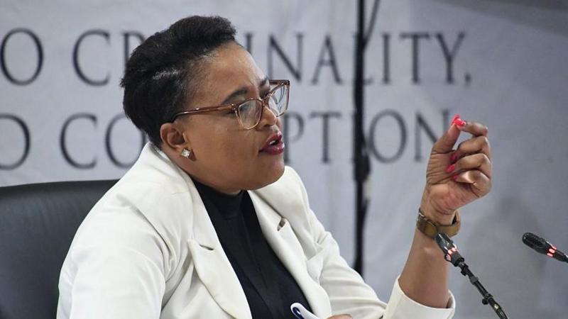 Brig Rachel Matjeng dressed in a white jacket and dark top underneath speaks into a microphone. Behind her, out of focus, is the banner for the Madlanga Commission.