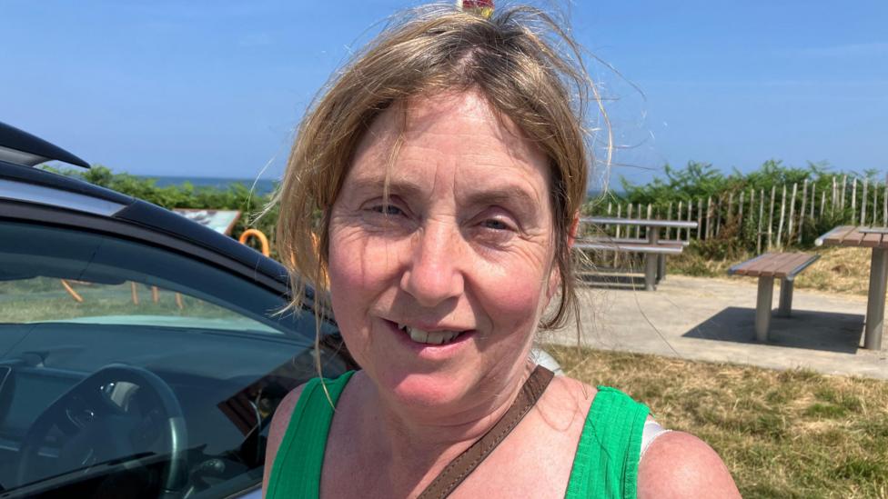 Sophia Hegarty is standing beside her car in a green top and has long blonde hair. 
