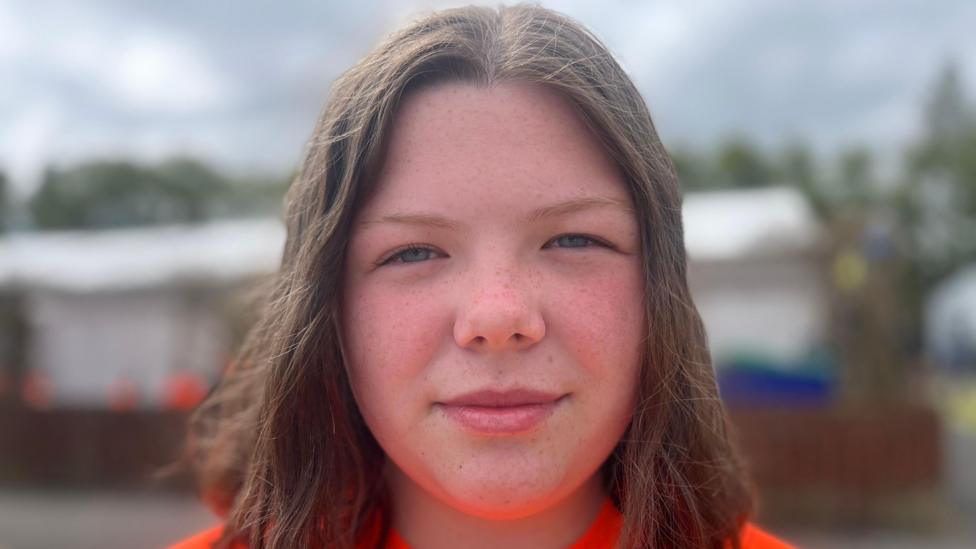 A girl with dark hair wearing an orange top