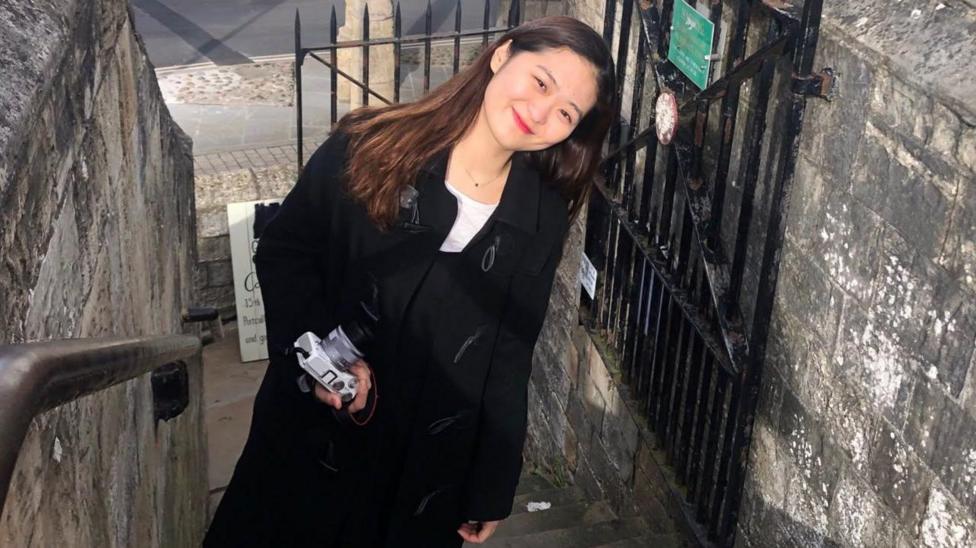 Jacqueline Choi, 28, poses for a picture, smiling as she leans towards her left.