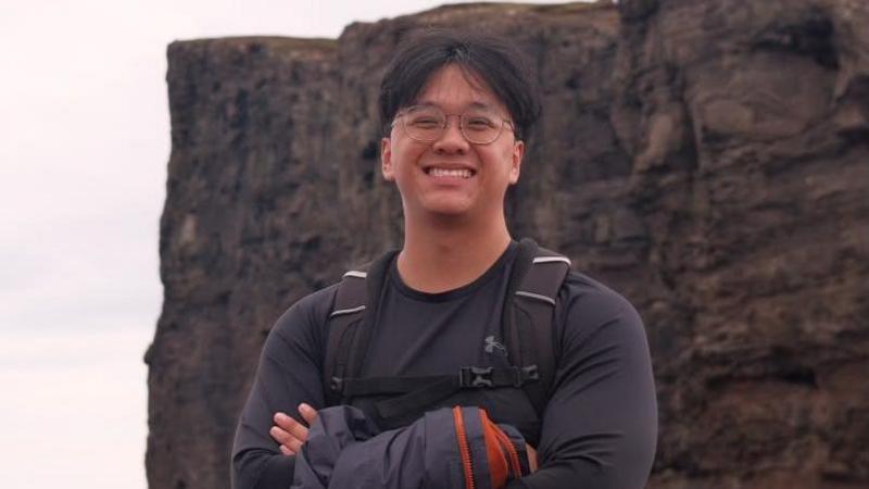 Shyan Lim smiling for a picture with his arms crossed during a hike near a cliff