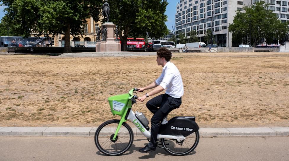 A man on an electric bike cycles past a patch of dry, brown grass
