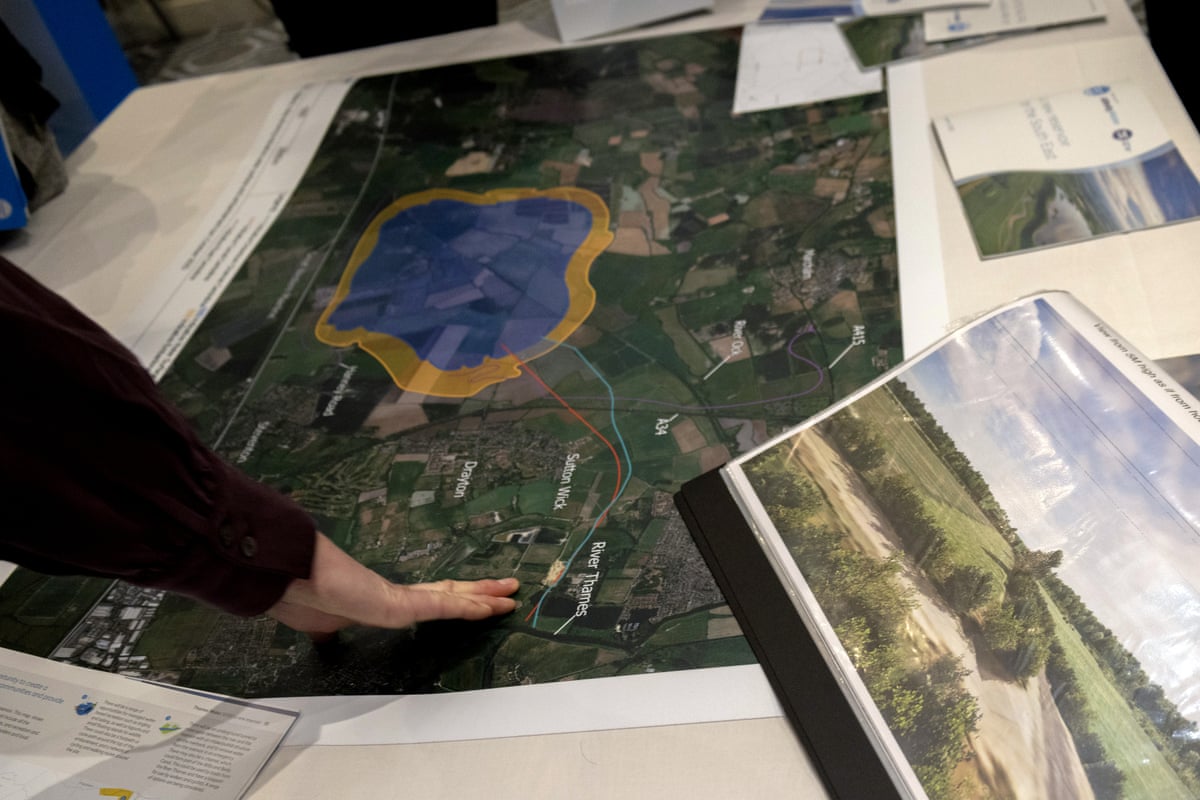 An anonymous hand reaches out to a map and other plans for a reservoir laid out on a table