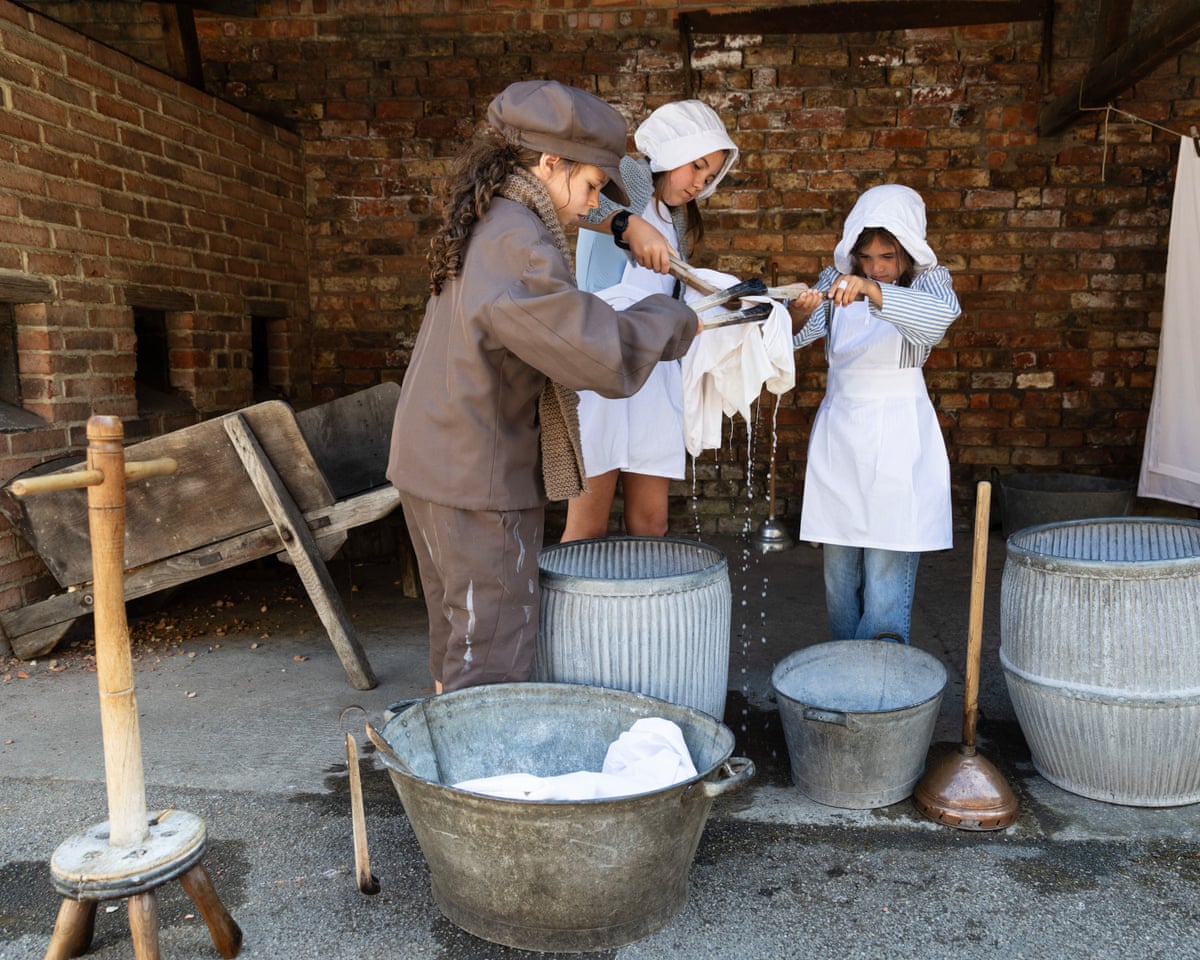 Three children in Victorian dress wash clothes in metal tubs