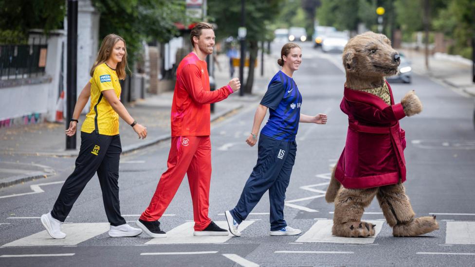 Sophie Munro, Phil Salt, Liv Barnes and a meerkat mascot walk across a pedestrian crossing