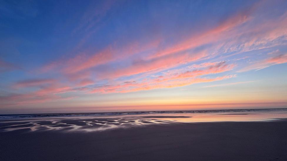 Pink and blue sunset reflected across wet beach sand.