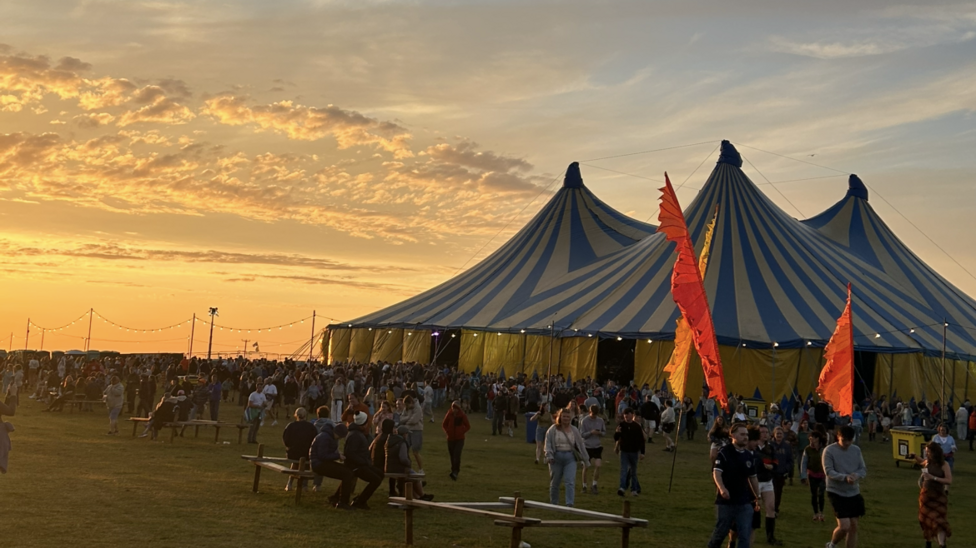 Large striped festival tent at sunset with crowds gathering.