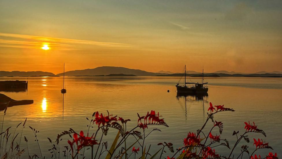 A fishing boat anchored on calm water at sunset.
